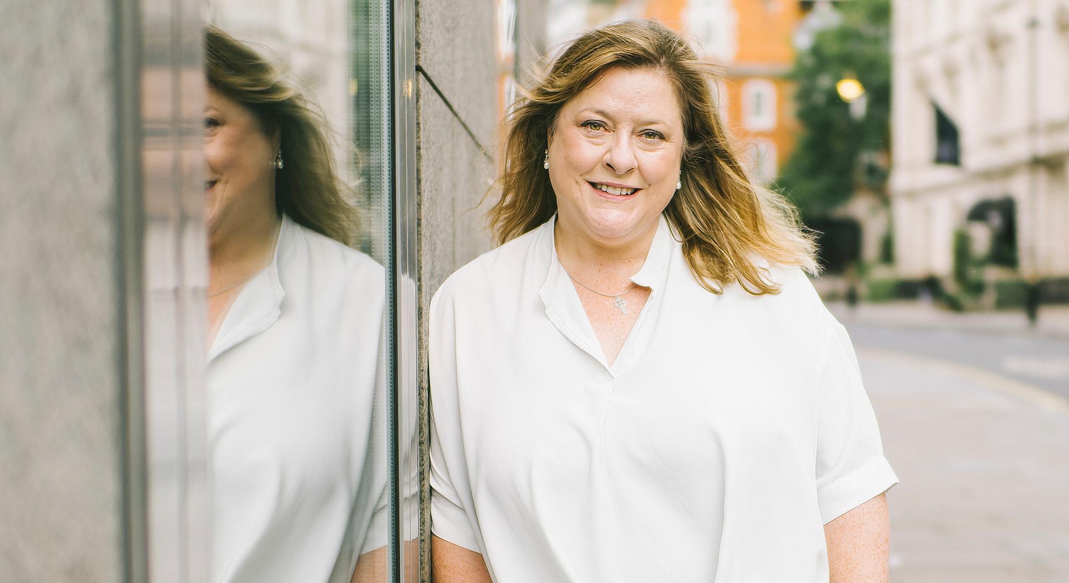 Smiling woman standing beside a reflective surface.