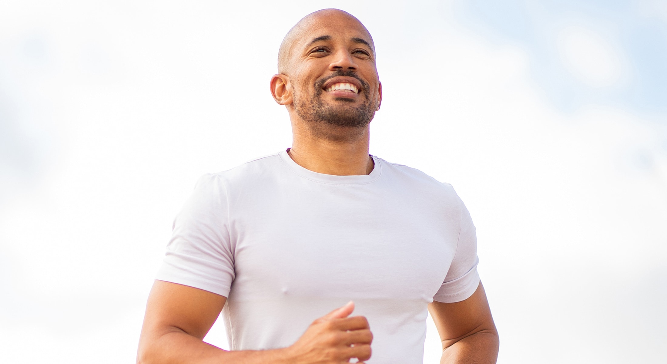 Smiling man jogging outdoors in daylight.